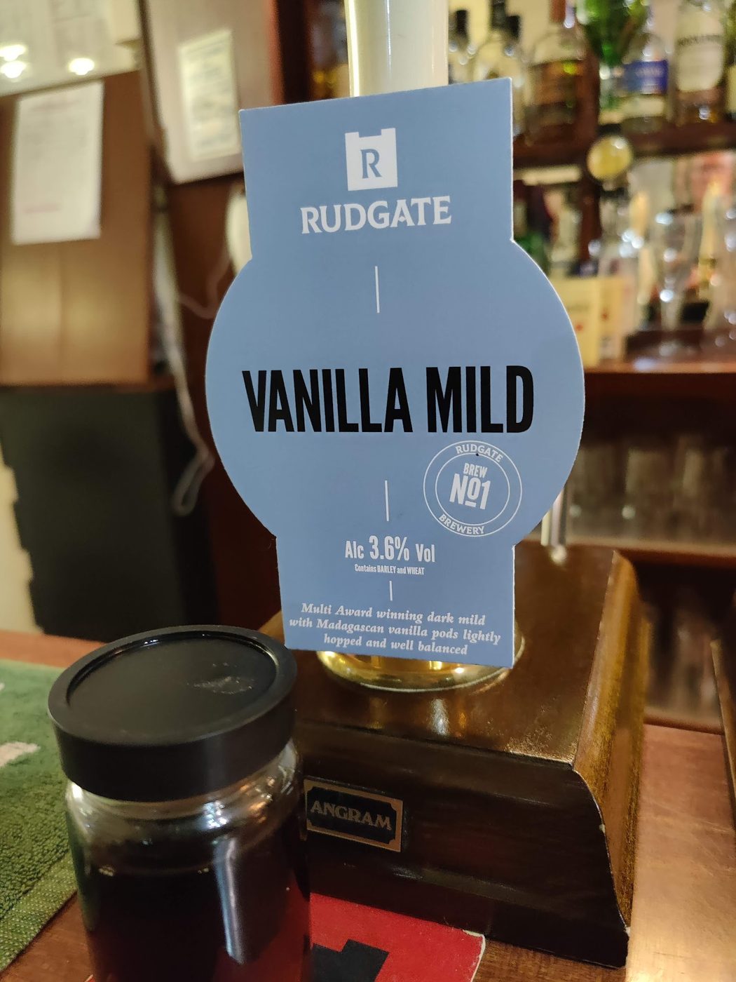 A Rudgate Vanilla Mild pump clip with a glass of dark ale